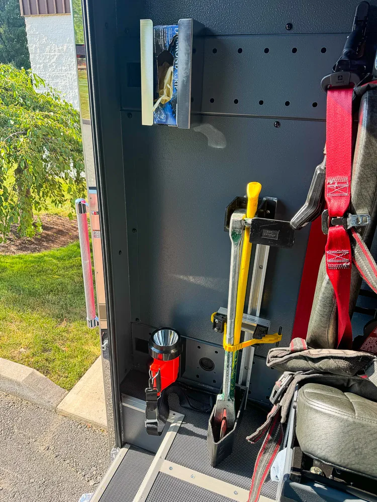 Rear cab interior doorway view showing mounted hand tool, seat harness, and interior storage points.