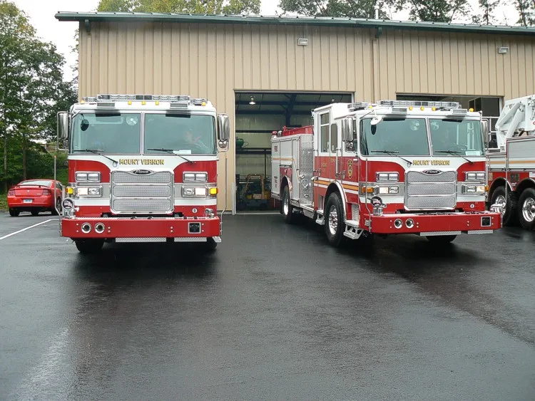 Head-on front lineup view of two pumpers parked in front of a station bay.