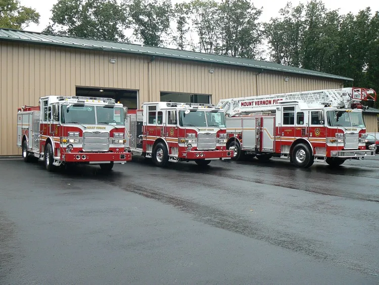 Three-truck lineup view showing two pumpers and a ladder truck parked side-by-side.
