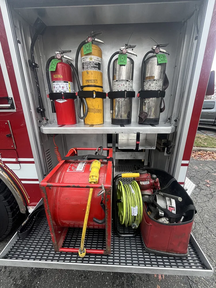 Open side compartment showing mounted extinguishers and hose reel storage