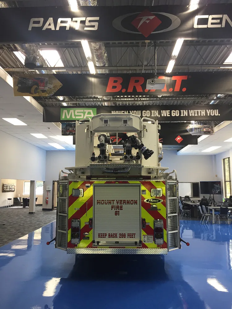 Straight rear view with red-yellow chevrons, rear roll-up door, and elevated platform nozzle assembly.