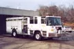 Wide front right view of the parked pumper with bumper, cab, and side compartments visible.