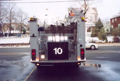 Straight rear view showing loaded hosebed, rear step platform, and tail lights.