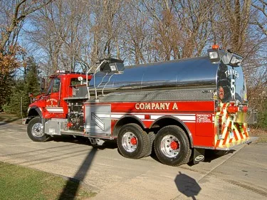 Rear-right exterior view showing cylindrical tank, tandem rear axles, and rear chevrons