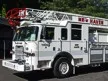 Wide front-left view of the ladder truck parked near trees with full side body visible.