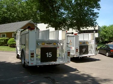 Rear view of both apparatus showing tailboard sections, rear warning lights, and unit number panels.