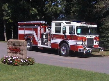 Front-left wide view of the pumper parked near the entrance sign with full side profile visible.