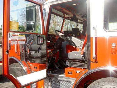 Open driver door interior view showing steering wheel, pedals, and dashboard controls