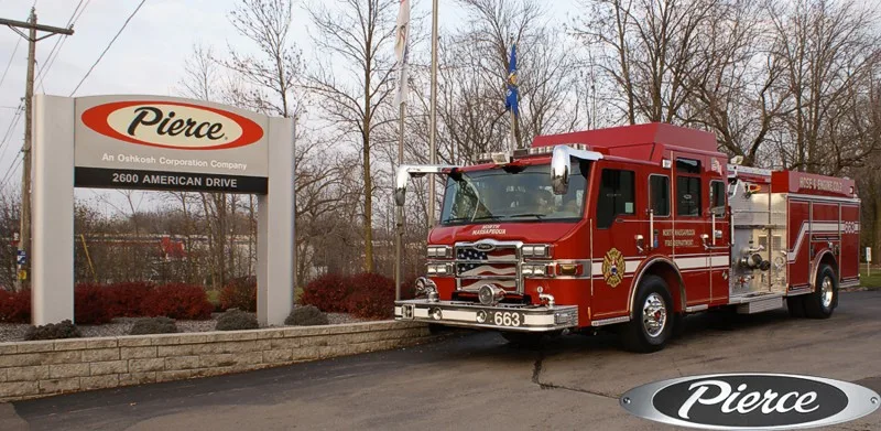 Front-left wide view of the pumper by the sign showing full cab and rear body compartments.