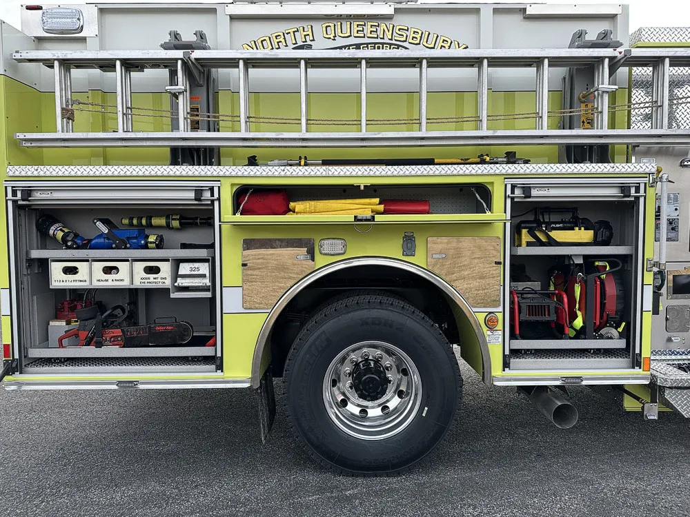 Driver-side mid-body view with open compartments showing chainsaw, nozzles, and tool storage