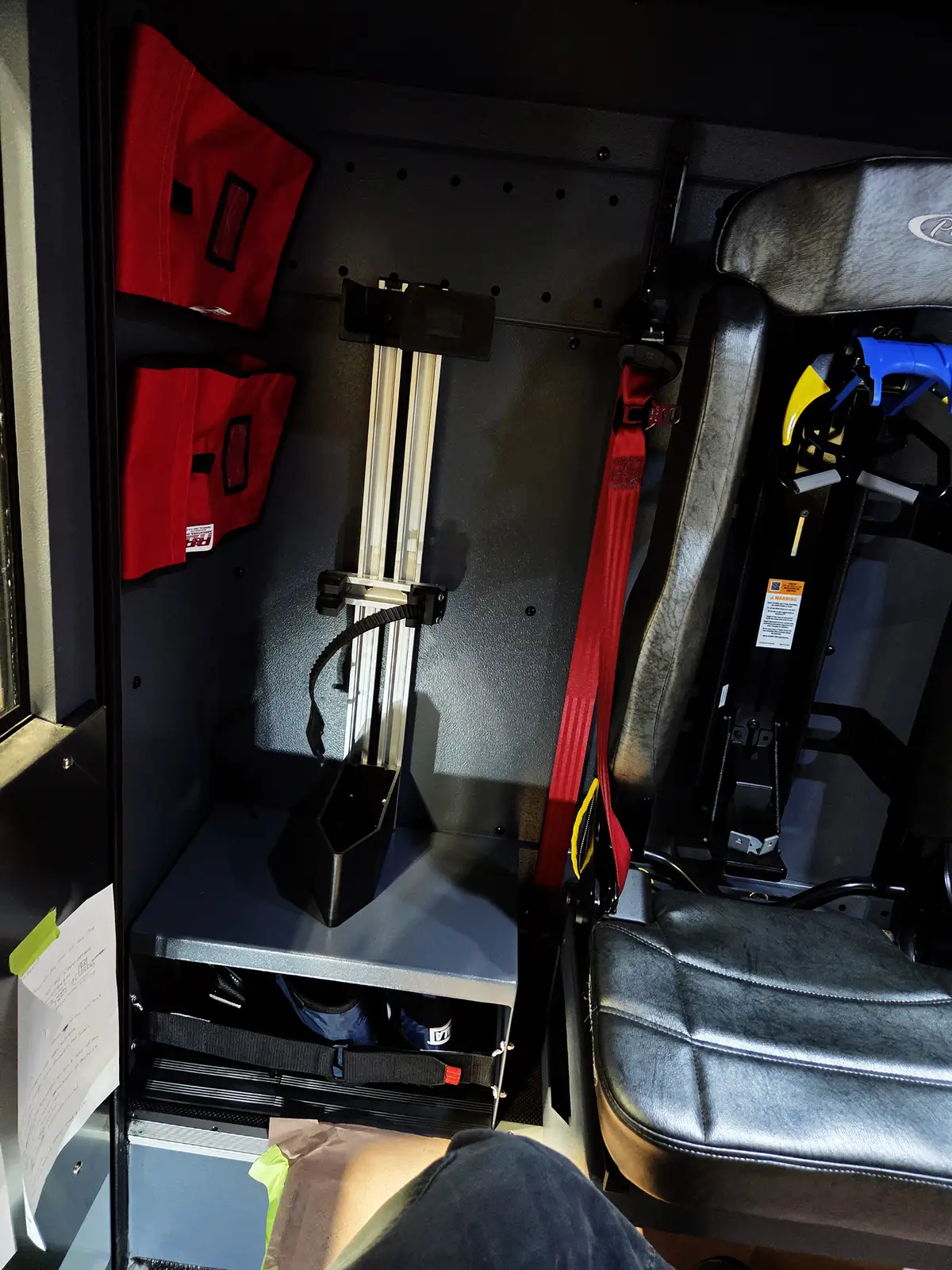 Interior crew-seat area view showing seat mount, red restraint, and storage shelf