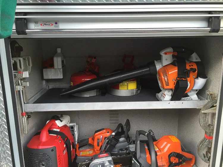 Open equipment compartment showing chainsaws, blower, and fuel containers