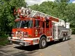 Aerial ladder truck front-left exterior view showing enclosed cab and ladder bed