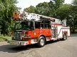 Wide front left view of the parked aerial ladder truck showing cab, bumper, and ladder bed.