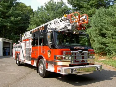 Front right angle showing chrome grille, cab roof lights, and stowed aerial ladder above the cab.