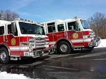 Wide side-front view of two red-and-white pumpers parked together on wet pavement.
