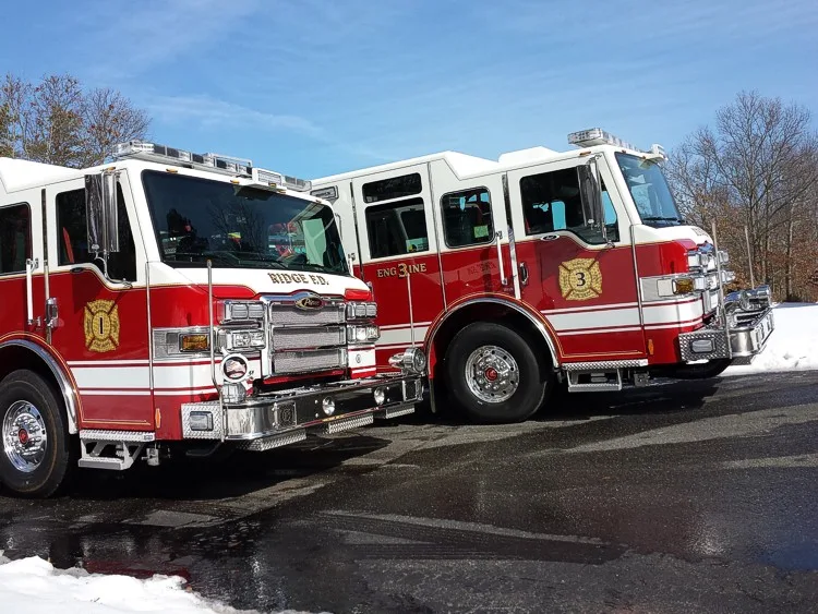 Front three-quarter view of two red-and-white pumpers parked side by side with matching chrome front ends.