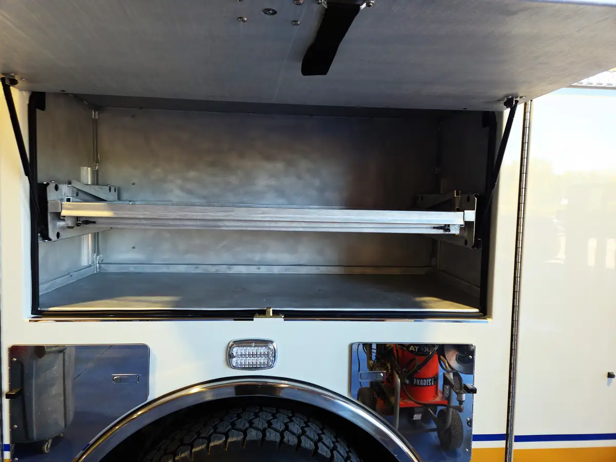 Open upper compartment above rear wheel showing empty shelving and slide tracks