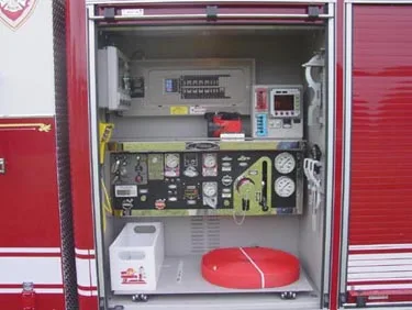 Pump panel compartment close-up showing gauges, valves, control levers, and hose connections