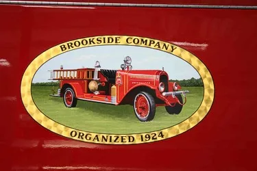 Close-up of an oval side logo featuring a vintage fire engine illustration and gold border.