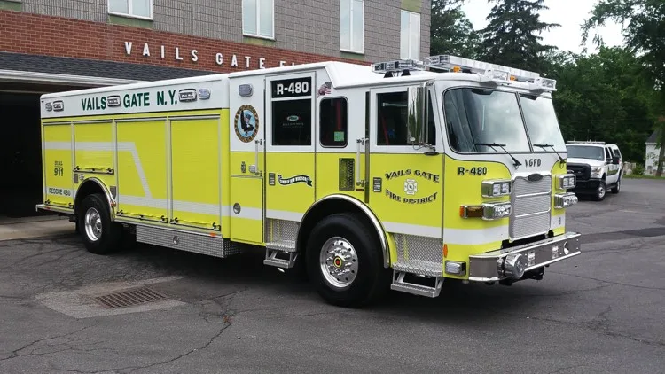 Front-right exterior view showing the rescue pumper cab face, side compartment layout, and rear wheel area.