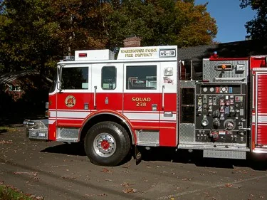 Driver-side cab and pump panel close-up showing gauges, valve controls, and front wheel area.