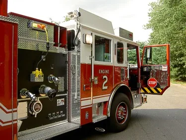 Driver-side pump panel view showing gauges, hose connections, and open cab door