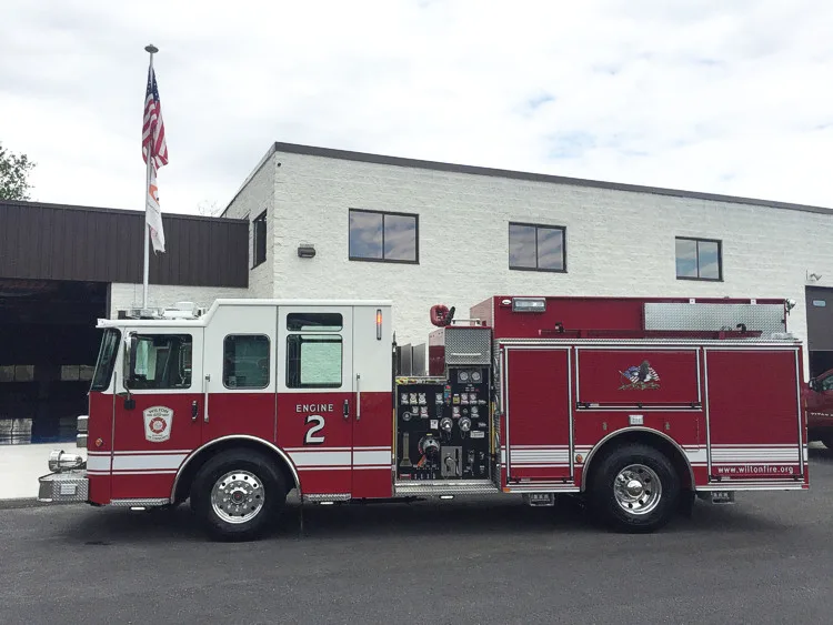 Full right-side profile parked by a building, showing pump panel controls and body compartments.