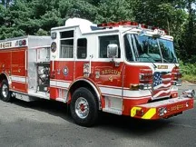 Wide front-right view of the rescue pumper parked by the building with full side body visible.