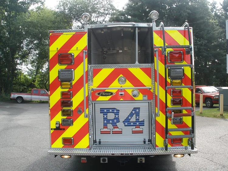 Straight rear view with red-yellow chevrons, rear ladder, rear warning lights, and top storage opening.