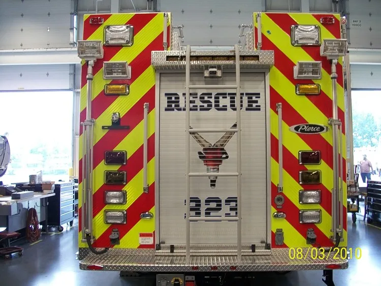 Straight rear view with red-yellow chevrons, rear ladder, and center rear roll-up door.