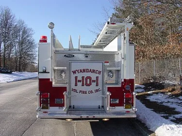 Straight rear view showing rear roll-up door, upper hosebed ladder section, and corner warning lights.