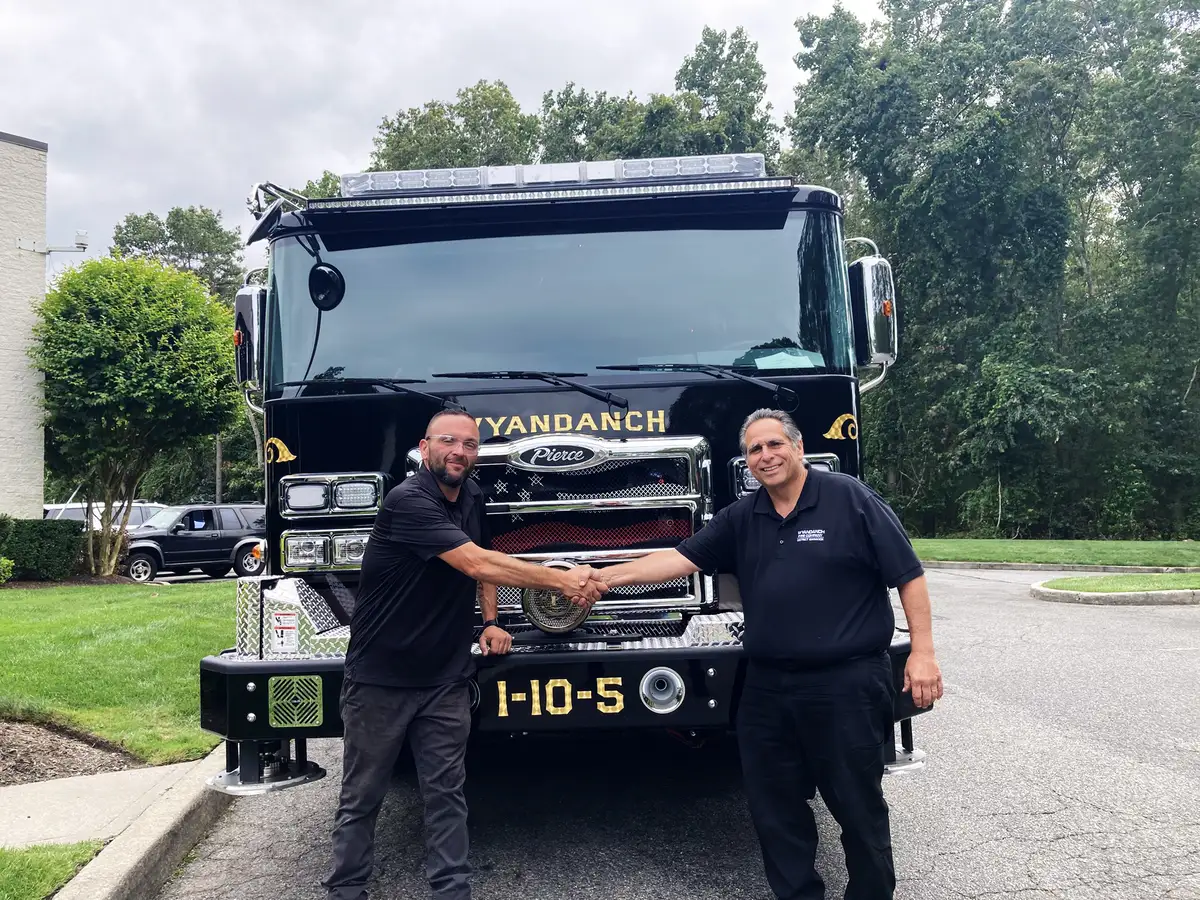 Front view with two people shaking hands in front of cab and bumper