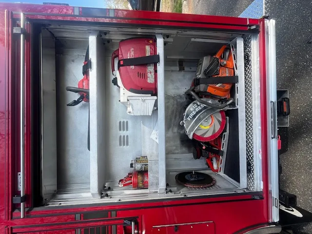 Open side compartment showing chainsaws, rescue saw, and tool storage shelves